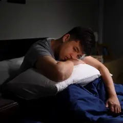 En man ligger i sängen, ser ut att kämpa med depression eller utmattning. Klockan på nattduksbordet visar att natten är lång.