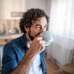 Man med lockigt hår dricker kaffe, blicken fundersam. Kanske en stund av kaffe ångest innan dagen börjar.