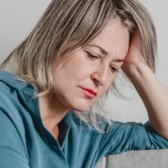En kvinna med handen mot huvudet, blicken sänkt. Hon utstrålar en känsla av emotionell utmattning.