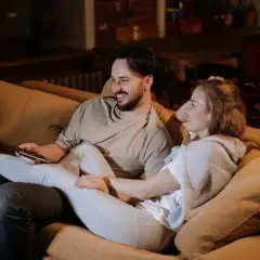 Ett par myser i soffan, skrattar och tittar på TV. Deras närhet och gemensamma skratt är grundstenar i en relation.