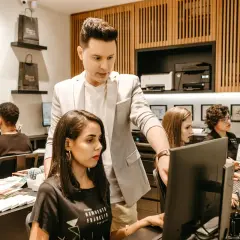 En narcissistisk kock, klädd i ljus kavaj, övervakar sitt team vid datorer.