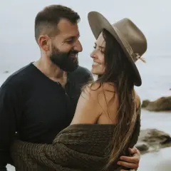 Ett par omfamnar varandra vid havet, deras blickar möts i en tydlig attraktion mellan två personer.