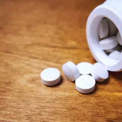 Vita tabletter, medicin mot panikångest, ligger utspridda på ett träbord bredvid en vit burk.