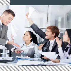 Business people in a meeting looking stressed and arguing, with papers flying.