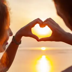 Ett par formar ett hjärta med händerna mot en solnedgång, en symbol för olika typer av relationer.