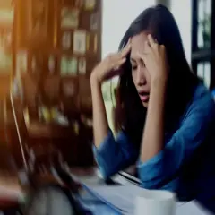 A woman with her hands on her head, looking distressed at a desk.