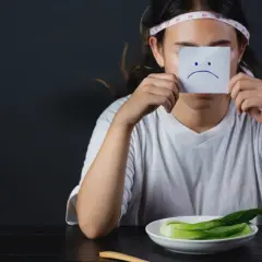 En person med måttband runt huvudet håller upp en lapp med ett ledsamt ansikte, en bild av ananke ocd.