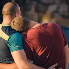 Två män omfamnar varandra. Den ena vilar huvudet mot den andras axel, en bild av en varaktig relation.