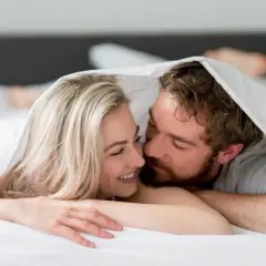 Ett par under täcket, hon ler, han viskar. Kanske en stund av ångest efter sex, eller bara intimitet.