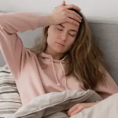 En kvinna med handen mot pannan i sängen, en känsla av ångest på morgonen.