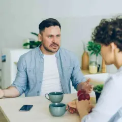 Man med intensiv blick förklarar något för kvinna, kanske om vad betyder narcissist. De sitter vid ett bord med kaffekoppar.