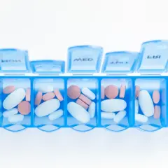 En blå medicindosa fylld med vita och rosa piller. Kan symbolisera hantering av mediciner och potentiella nackdelar med betablockerare.