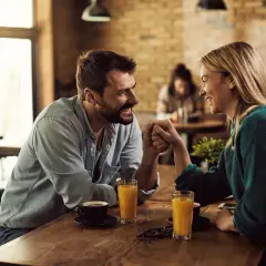 Ett par håller varandra i händerna vid ett bord på ett café, leende och ställande frågor till partner.