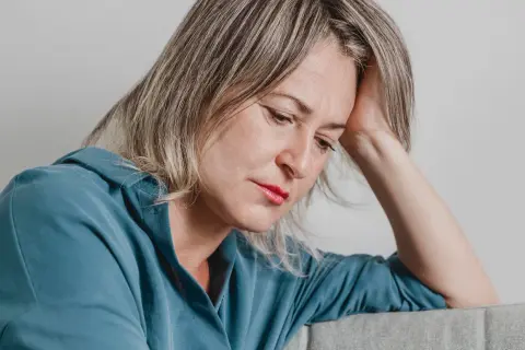 En kvinna med handen mot huvudet, blicken sänkt. Hon utstrålar en känsla av emotionell utmattning.