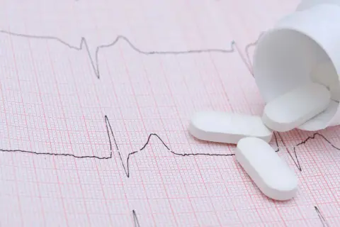 Vita tabletter, potentiellt betablockerare ångest, ligger utspridda på ett EKG-papper.