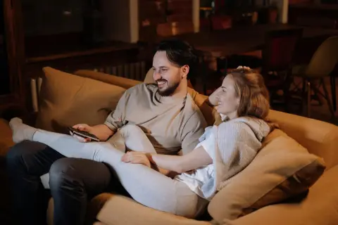 Ett par myser i soffan, skrattar och tittar på TV. Deras närhet och gemensamma skratt är grundstenar i en relation.