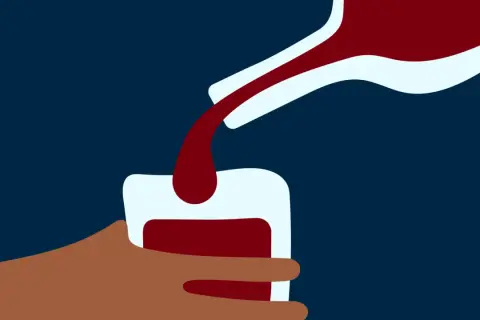 En hand håller ett glas medan mörkt vin hälls upp. En bild som kan symbolisera alkoholist beteende.