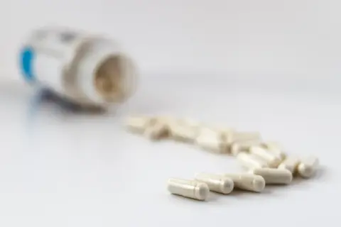 En burk med litiummedicin och flera kapslar utspridda på en vit yta.