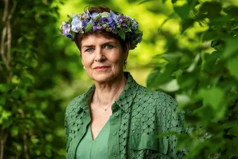 Ullakarin Nyberg med blomsterkrans i grönska.