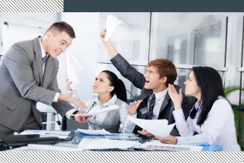 Business people in a meeting looking stressed and arguing, with papers flying.