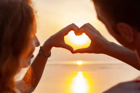 Ett par formar ett hjärta med händerna mot en solnedgång, en symbol för olika typer av relationer.