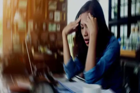 A woman with her hands on her head, looking distressed at a desk.