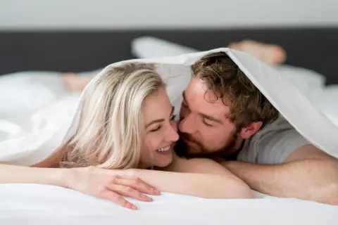 Ett par under täcket, hon ler, han viskar. Kanske en stund av ångest efter sex, eller bara intimitet.