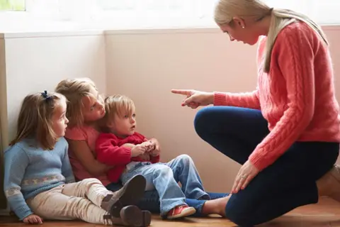 Kvinna pekar på barn som sitter på golvet. Kanske ett svårt samarbetssamtal med narcissist.