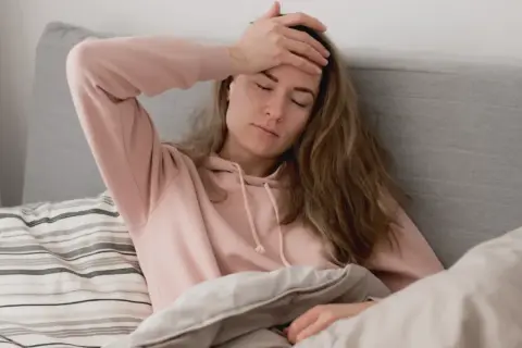 En kvinna med handen mot pannan i sängen, en känsla av ångest på morgonen.