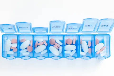 En blå medicindosa fylld med vita och rosa piller. Kan symbolisera hantering av mediciner och potentiella nackdelar med betablockerare.