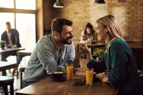 Ett par håller varandra i händerna vid ett bord på ett café, leende och ställande frågor till partner.