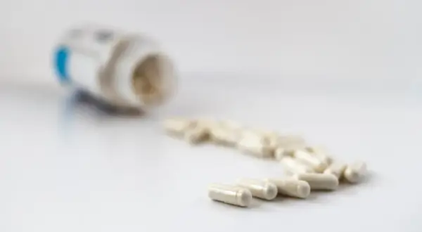 En burk med litiummedicin och flera kapslar utspridda på en vit yta.