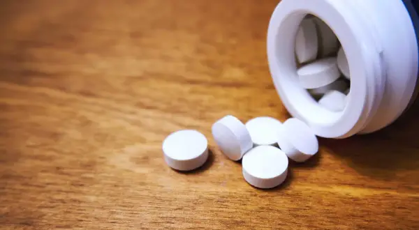 Vita tabletter, medicin mot panikångest, ligger utspridda på ett träbord bredvid en vit burk.