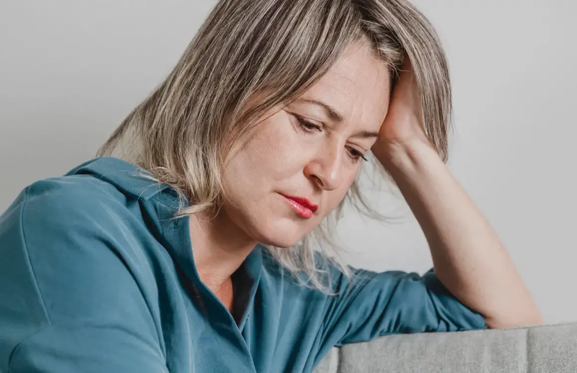 En kvinna med handen mot huvudet, blicken sänkt. Hon utstrålar en känsla av emotionell utmattning.