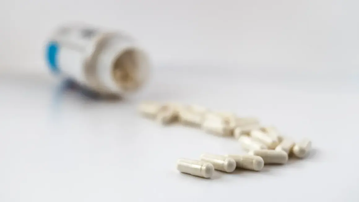 En burk med litiummedicin och flera kapslar utspridda på en vit yta.