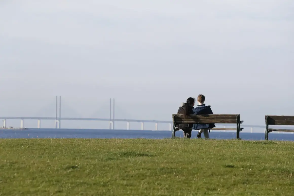 Två personer sitter på en bänk med Öresundsbron i bakgrunden. Kanske funderar de på vårdval psykoterapi.