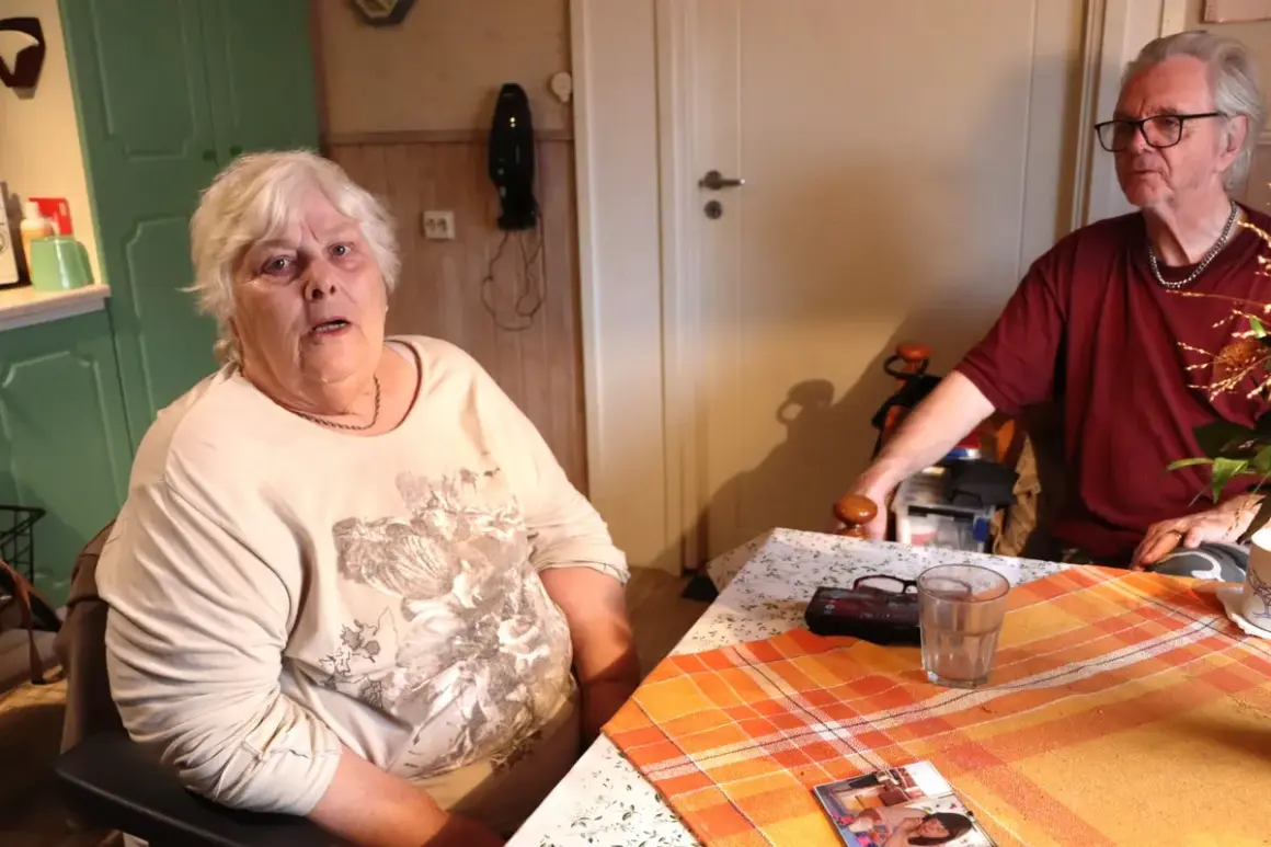En kvinna med vitt hår sitter vid ett bord. Hon ser trött ut, som om hon inte orkar med sin dementa mamma. En man sitter mittemot.