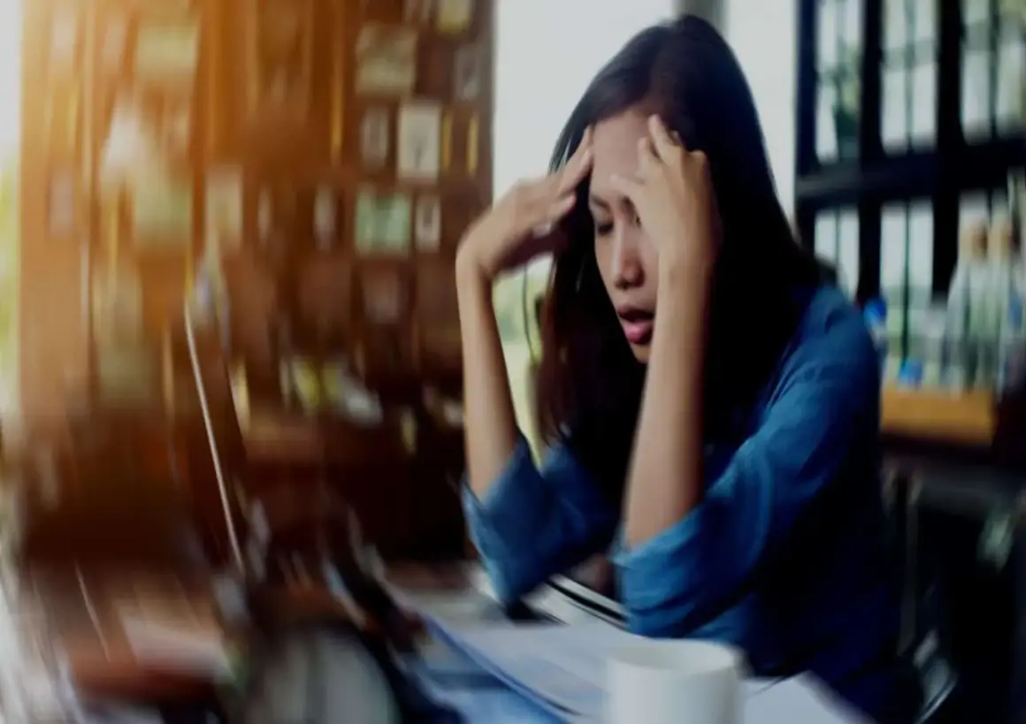 A woman with her hands on her head, looking distressed at a desk.