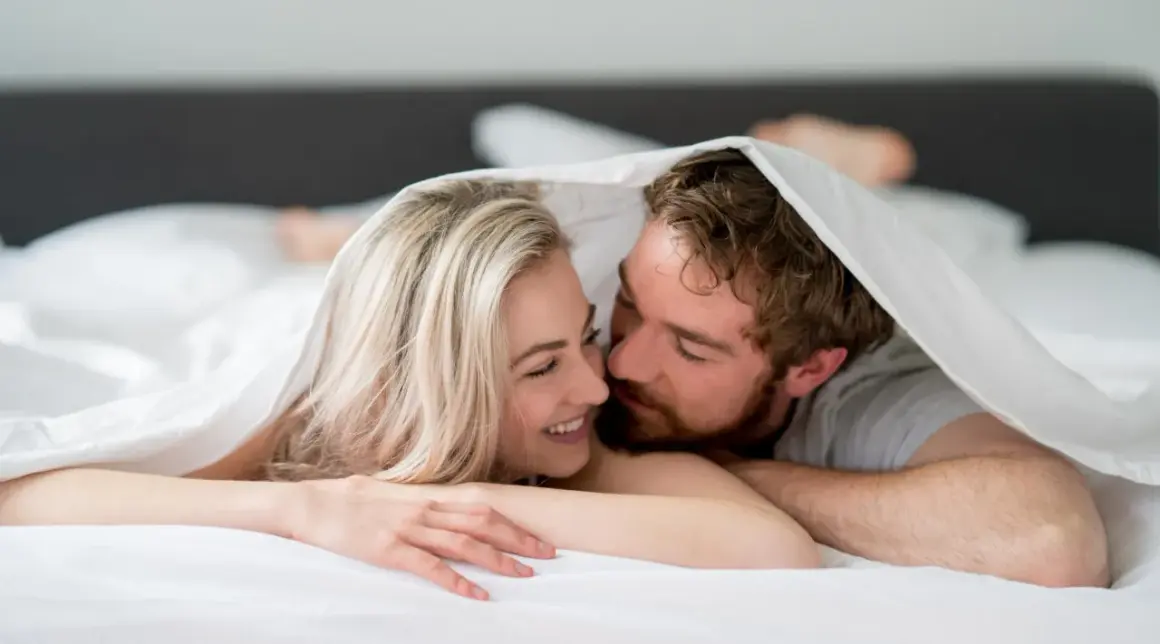Ett par under täcket, hon ler, han viskar. Kanske en stund av ångest efter sex, eller bara intimitet.