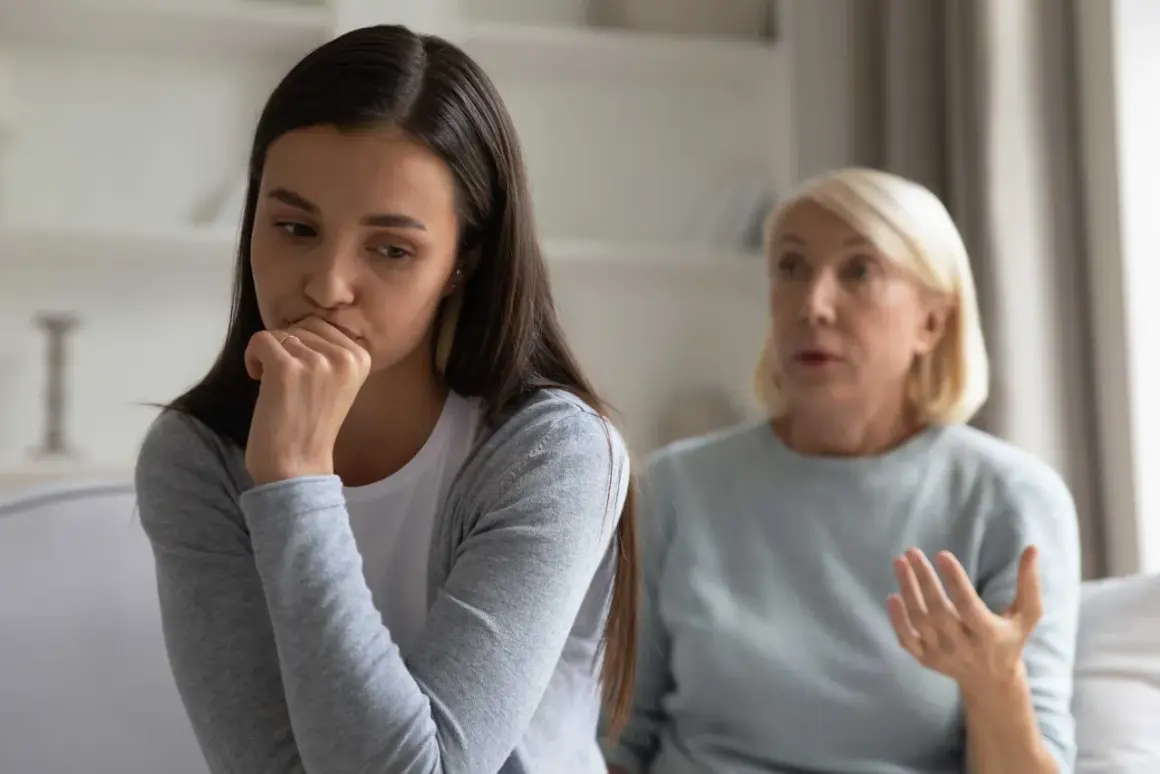 En ung kvinna sitter med handen mot munnen, ser bekymrad ut. Bakom henne gestikulerar en äldre kvinna, kanske en diskussion om ett problem med vuxen dotter.