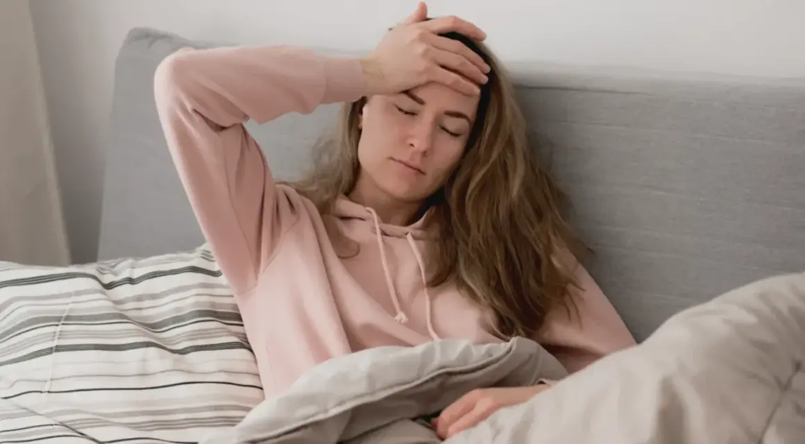 En kvinna med handen mot pannan i sängen, en känsla av ångest på morgonen.