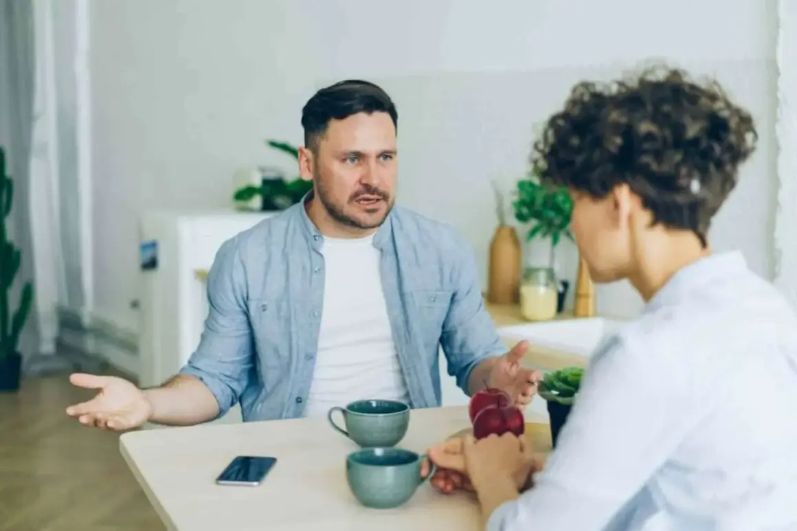 Man med intensiv blick förklarar något för kvinna, kanske om vad betyder narcissist. De sitter vid ett bord med kaffekoppar.