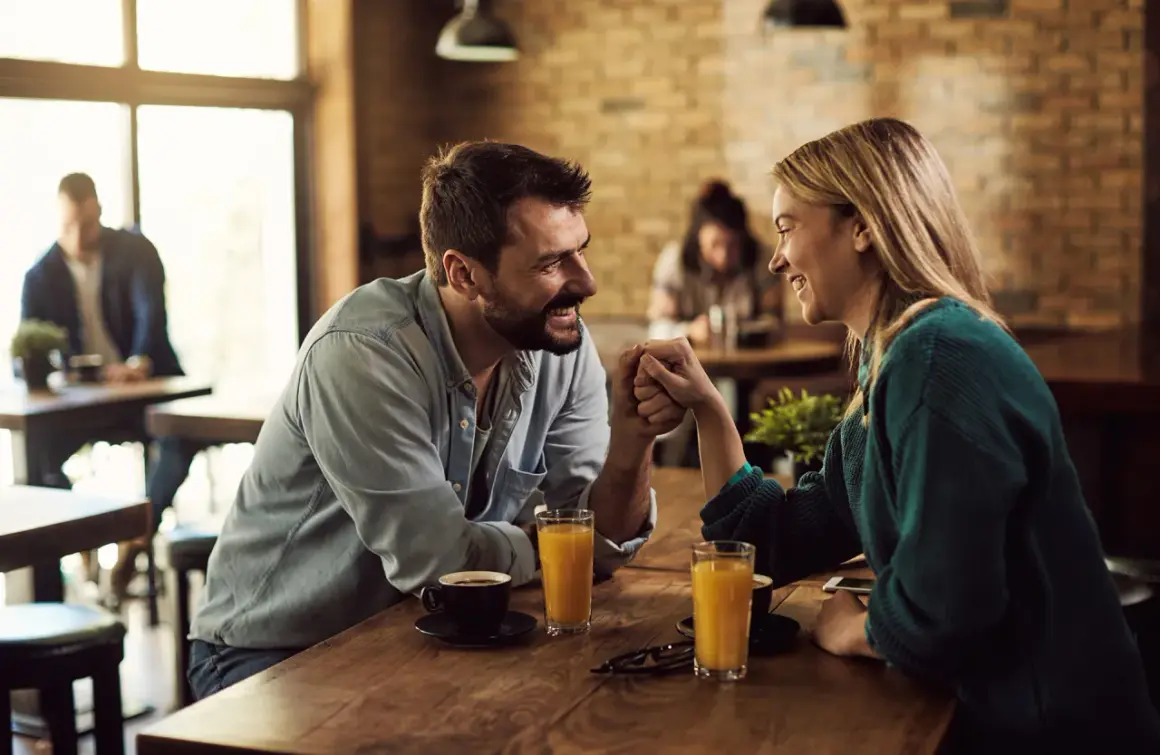 Ett par håller varandra i händerna vid ett bord på ett café, leende och ställande frågor till partner.
