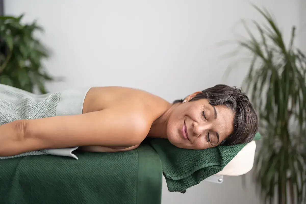 En kvinna vilar på en massagebänk, med slutna ögon och ett fridfullt leende. En ny början, livet efter utmattningssyndrom.
