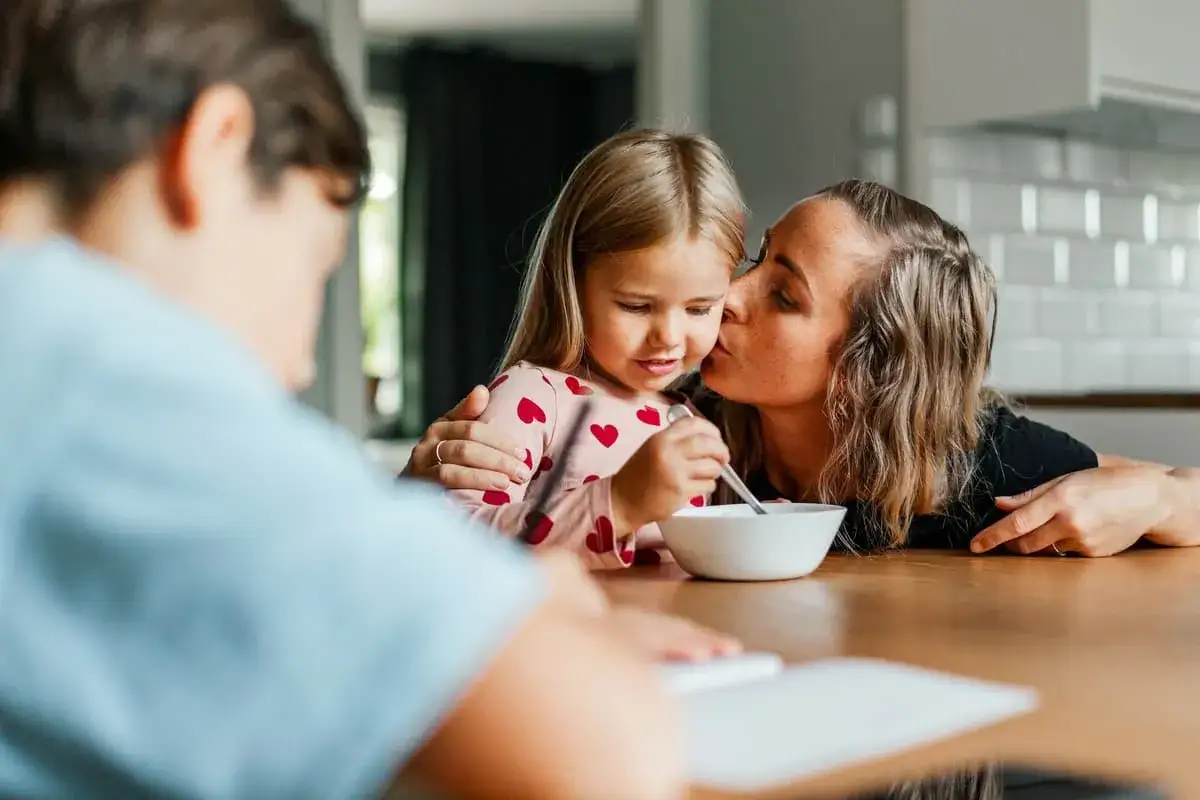 Mamma ger sin dotter en kyss p&aring; kinden medan hon &auml;ter frukost. En fin stund att prata med barn.