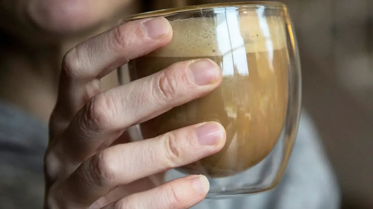 En hand håller ett glas med kaffe. Kanske dags att sluta med kaffe depression och hitta nya rutiner.